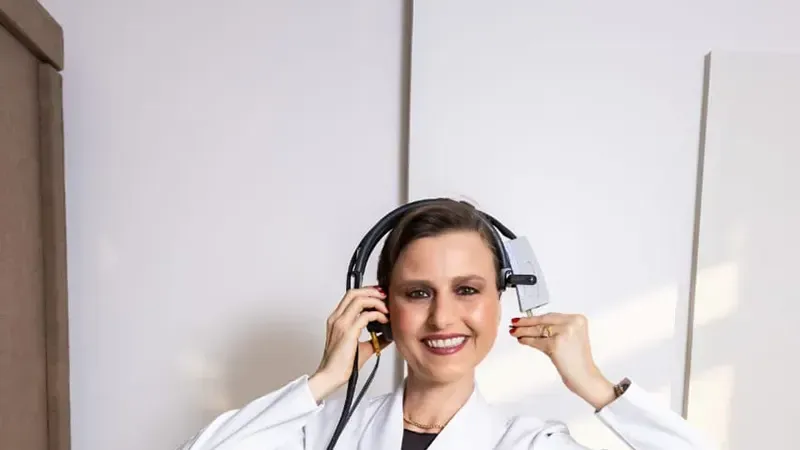 Fonoaudióloga do INAB com fone de exame auditivo ao lado do equipamento de impedanciometria